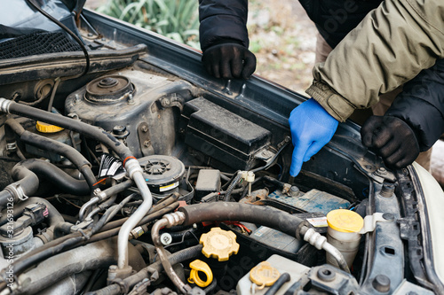 Two Car mechanic engineers checking, fixing the car, making maintenance comprehensive auto check. Auto mechanic in blue gloves detected breakdown and indicates a malfunction. Car repair service