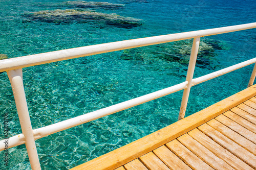 summer time wooden pier white pipe fence outdoor view from above on transparent water of Red sea with coral reefs on bottom © Артём Князь