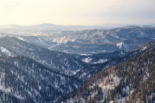 Winter mountain landscape. Snowy mountains at sunset, covered with coniferous forest. Russia. Altai Republic.