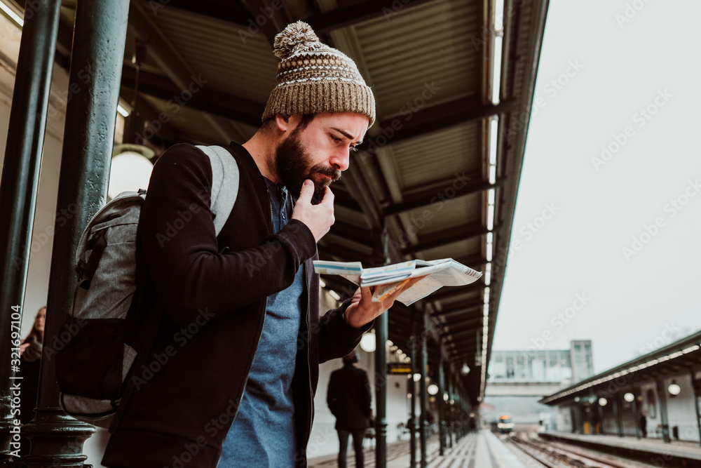 .Attractive young man with beard waiting at the train station in Vienna. Thinking about his trip, with the map in his hand a bit lost and worried. Travel photography.