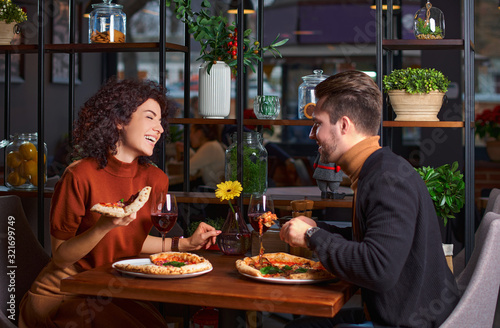 Young lovely couple is eating pizza it in pizzeria. guy is amuses his girl in a restaurant. Happy people having fun together