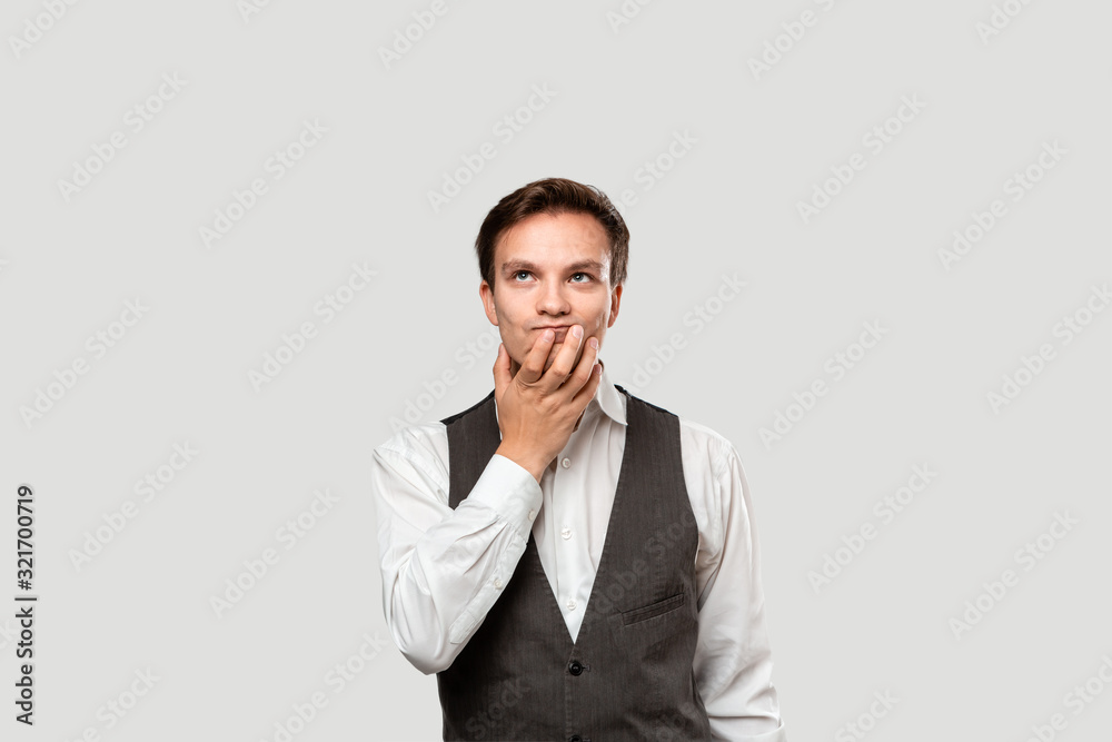 Thoughtful young businessman in a white shirt and grey vest holding chin on a palm of a hand Thoughtful young businessman in a white shirt and grey vest holding chin on a palm of a hand