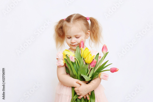 Little beautiful girl blonde with a bouquet of tulips on a light background. Baby girl smiling. Spring and women's day concept. Little girl holding a bouquet of colored tulips. Сopy spase