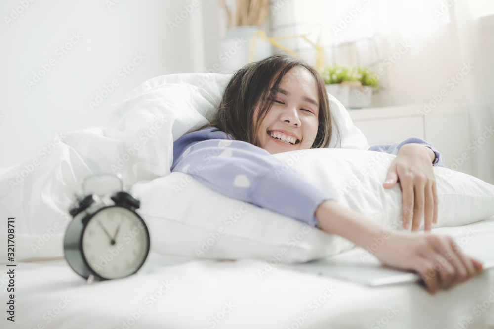 portrait happy young asian pretty woman in casual clothing smiling with tablet and alarm clock lying with pillow on bed in bedroom at home, lifestyle, good morning, holiday and joyful weekend concept - obrazy, fototapety, plakaty 