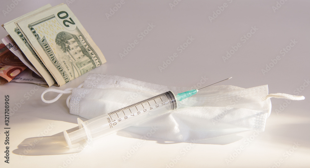 the syringe lies on a protective medical mask. Near a pack in dollars, euros, lira. White background. Concept - economic crisis, coronovirus, market crash, vaccine, crisis protection the syringe lies on a protective medical mask. Near a pack in dollars, euros, lira. White background. Concept - economic crisis, coronovirus, market crash, vaccine, crisis protection