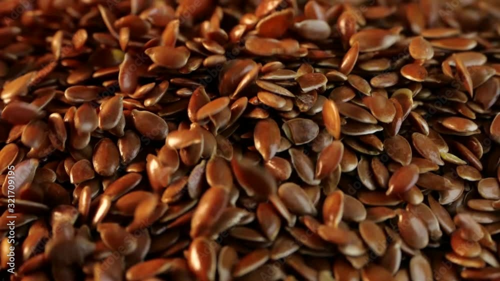 Many flax grains are poured onto the surface, and they create a hill. Close-up view of falling flax seeds on a black background in an isolated room in slightly slow motion. Product for weight loss. Many flax grains are poured onto the surface, and they create a hill. Close-up view of falling flax seeds on a black background in an isolated room in slightly slow motion. Product for weight loss.