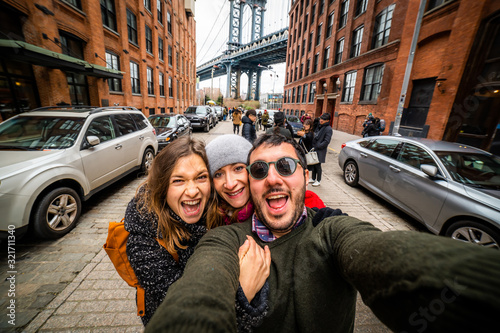 happy friends tourist taking selfie in Manhattan Bridge seen from Dumbo, Brooklyn, New York City, USA