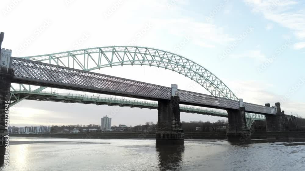 Aerial view arched green steel bridge & railway crossing over river reflections sunrise. Low dolly left pullback. Aerial view arched green steel bridge & railway crossing over river reflections sunrise. Low dolly left pullback.