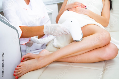 Laser hair removal of female legs. A cosmetologist removes hair with a laser device on the patient's legs.