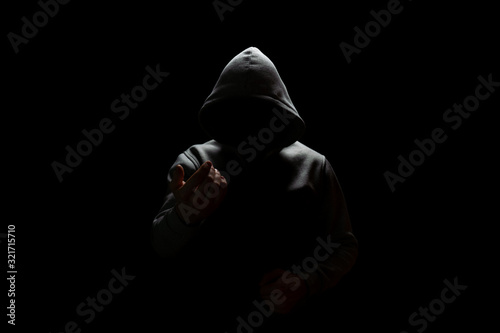 an unknown person in a hood lures into the darkness