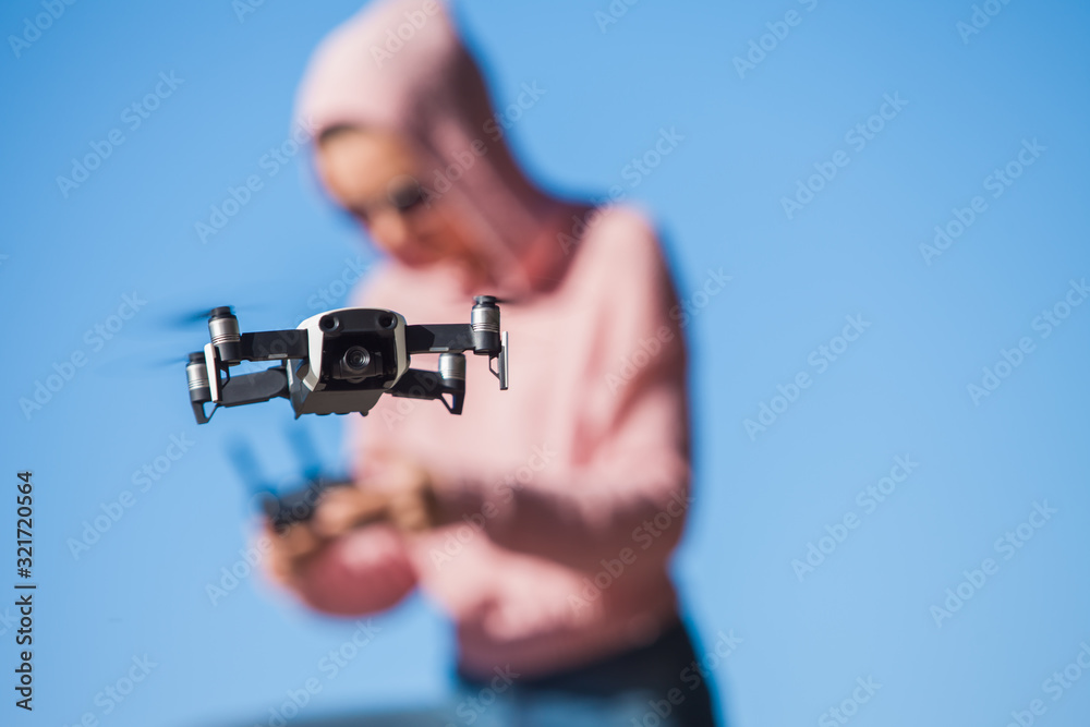 Standing with a bended knee, young woman in pink hoodie and dark glasses controls the drone's flight control panel. Standing with a bended knee, young woman in pink hoodie and dark glasses controls the drone's flight control panel.