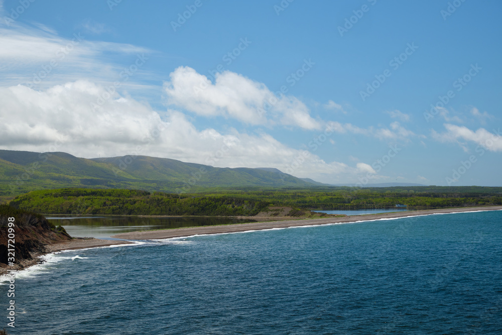 View on a lagoon, coastline of Nova Scotia and green forest. Blue cloudy sky and mountains.