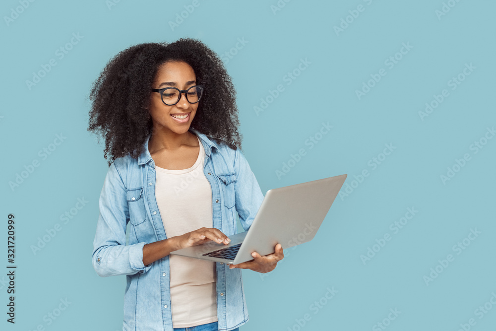 Freestyle. African girl in glasses standing isolated on gray browsing web on laptop smiling joyful Freestyle. African girl in glasses standing isolated on gray browsing web on laptop smiling joyful