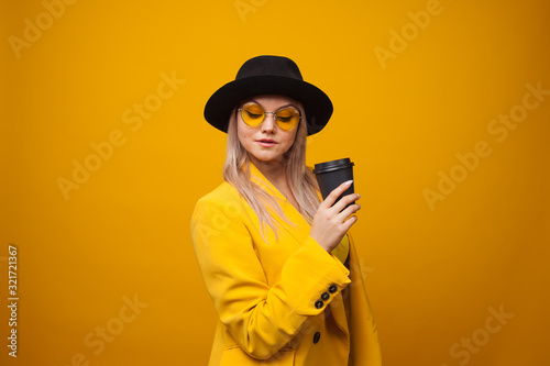 Take-away coffee. Stylish trendy young woman in bright clothes on a yellow background.