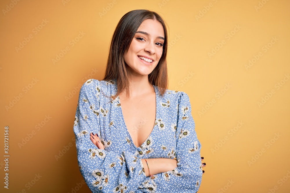Young beautiful brunette woman wearing casual floral t-shirt standing over yellow background happy face smiling with crossed arms looking at the camera. Positive person. Young beautiful brunette woman wearing casual floral t-shirt standing over yellow background happy face smiling with crossed arms looking at the camera. Positive person.