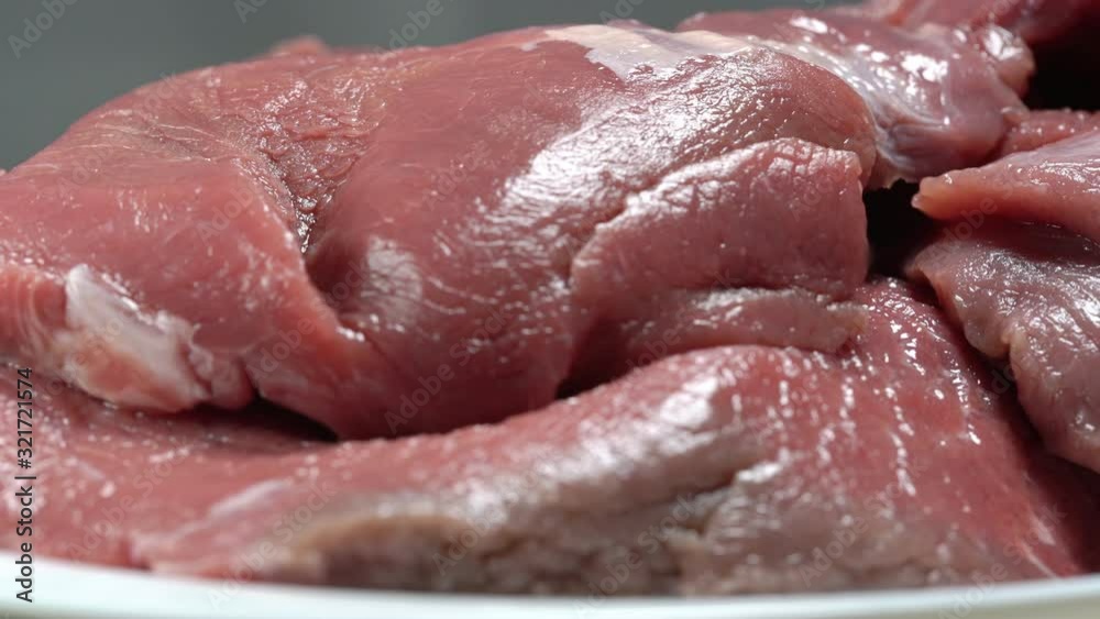 white plate with pieces of fresh raw juicy pork fillet meat turns at bright lamp light extreme close view