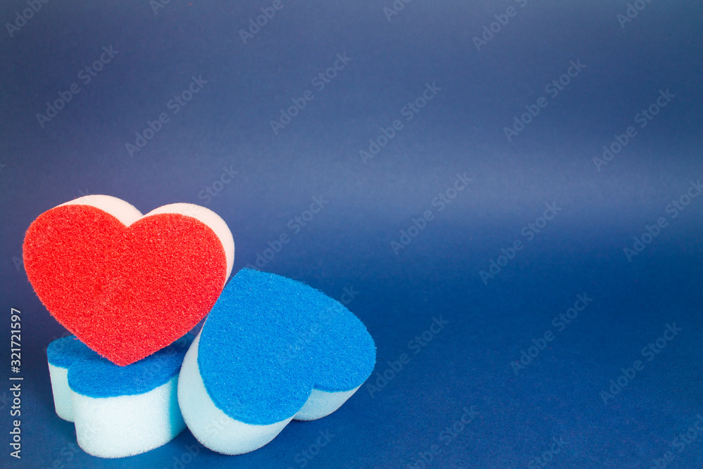 Obraz premium Red heart shape dishwash sponge over two blue heart shape dishwasher sponge in the foreground on the blue background