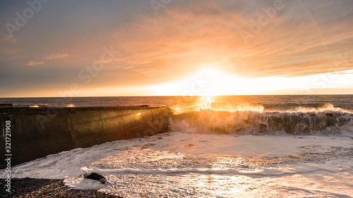 Big waves breaking on a stone pier in stormy weather with a bright sunset, a big tide. Black Sea. Sochi, February.