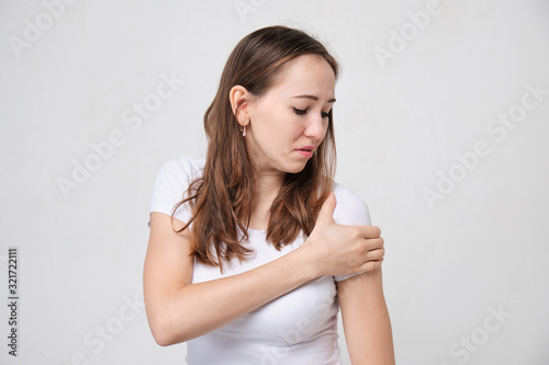 A girl in a white T-shirt massages her shoulder in pain.