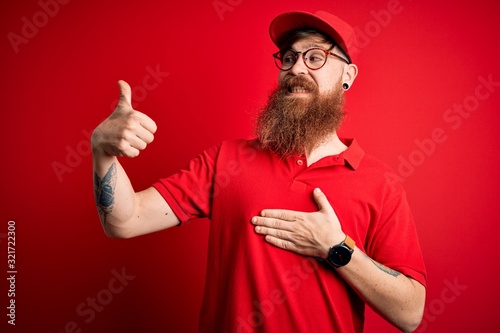 Young handsome delivery man wearing glasses and red cap over isolated background Looking proud, smiling doing thumbs up gesture to the side © Krakenimages.com
