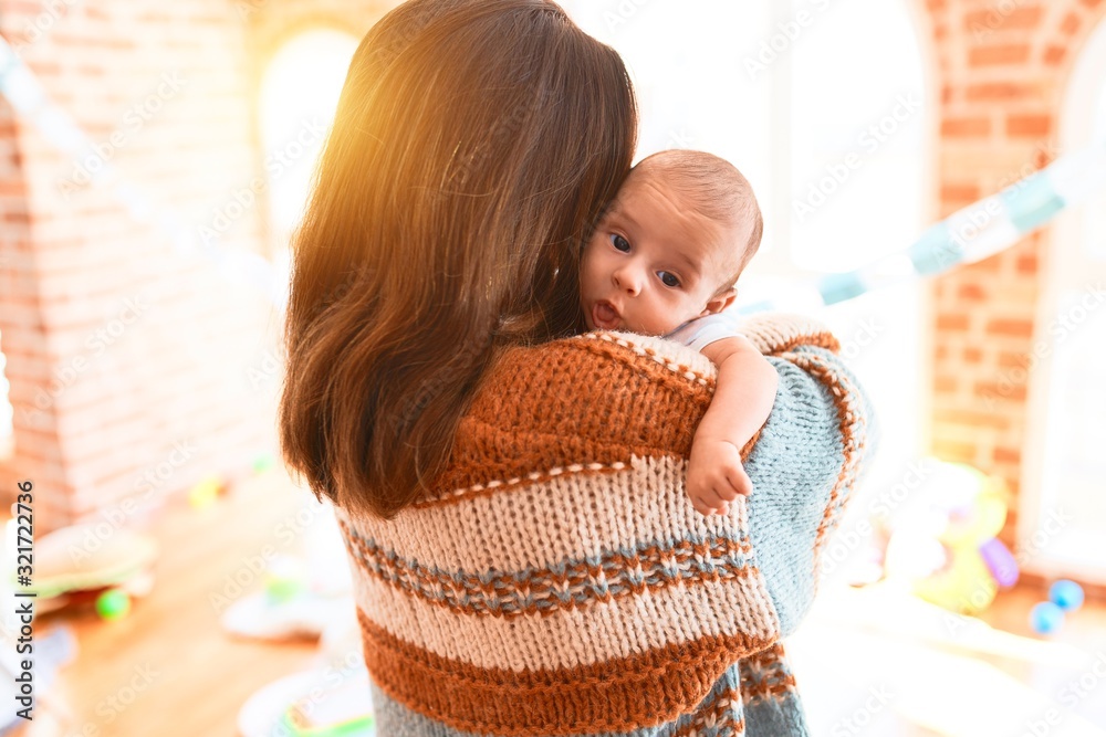 Fototapeta premium Young beautiful woman and her baby standing at home. Mother holding and hugging newborn