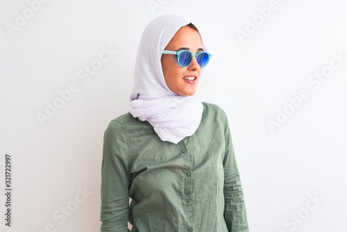 Young Arab woman wearing hijab and summer sunglasses over isolated background looking away to side with smile on face, natural expression. Laughing confident.