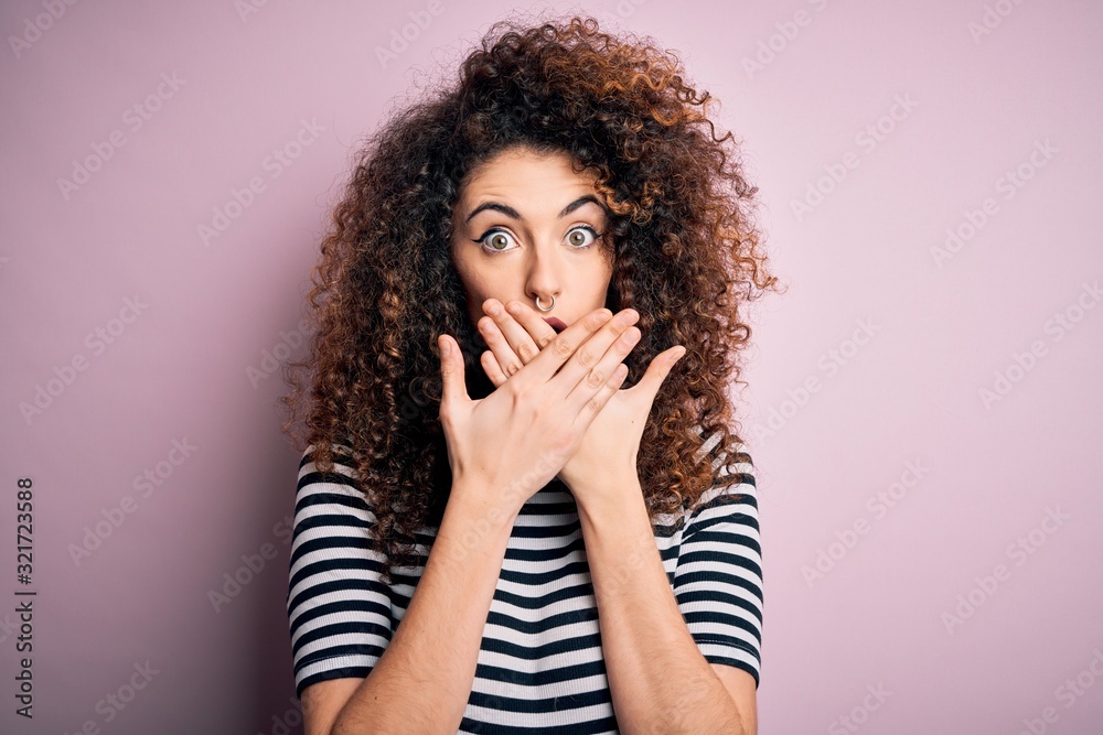 Young beautiful woman with curly hair and piercing wearing casual striped t-shirt shocked covering mouth with hands for mistake. Secret concept. Young beautiful woman with curly hair and piercing wearing casual striped t-shirt shocked covering mouth with hands for mistake. Secret concept.