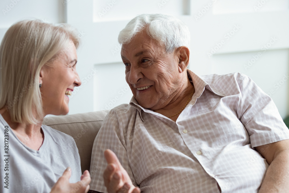 Happy mature husband and wife have fun talking on couch