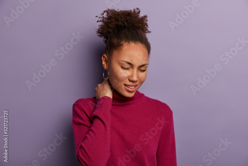 Stressed overworked freelancer suffers from osteohondrosis and neck pain, smirks face from pain, has problems with health, needs massage, wears casual clothes, feels exhuasted of working long time photo