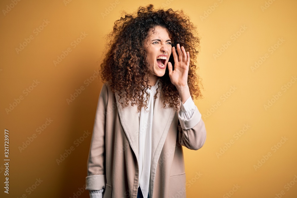 Young beautiful brunette woman with curly hair and piercing wearing casual t-shirt and diadem shouting and screaming loud to side with hand on mouth. Communication concept. Young beautiful brunette woman with curly hair and piercing wearing casual t-shirt and diadem shouting and screaming loud to side with hand on mouth. Communication concept.