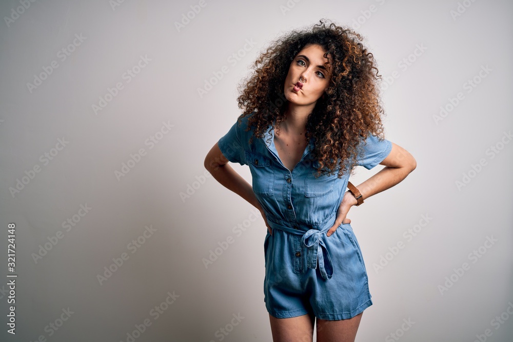Young beautiful woman with curly hair and piercing wearing casual denim dress making fish face with lips, crazy and comical gesture. Funny expression. Young beautiful woman with curly hair and piercing wearing casual denim dress making fish face with lips, crazy and comical gesture. Funny expression.