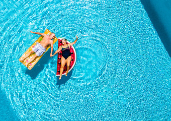 Vertical view of happy couple of old senior people enjoying the summer holiday vacation at the blue water pool with coloured treny lilos together with fun and love