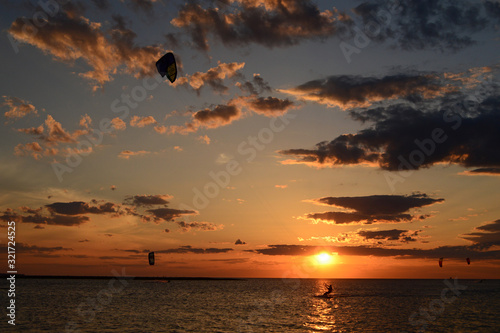 Obraz na plátně A kite surfer glides along an almost deserted bay as the sun sets