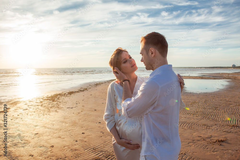 Love, waiting for the baby. Couple, pregnant woman and man, in white flying clothes, walk, hold hands, hug the tummy. Love, waiting for the baby. Couple, pregnant woman and man, in white flying clothes, walk, hold hands, hug the tummy.