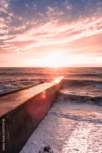 Big waves breaking on a stone pier in stormy weather with a bright sunset  a big tide. Black Sea. Sochi  February.