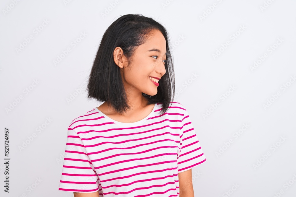 Young chinese woman wearing striped t-shirt standing over isolated white background looking away to side with smile on face, natural expression. Laughing confident. Young chinese woman wearing striped t-shirt standing over isolated white background looking away to side with smile on face, natural expression. Laughing confident.