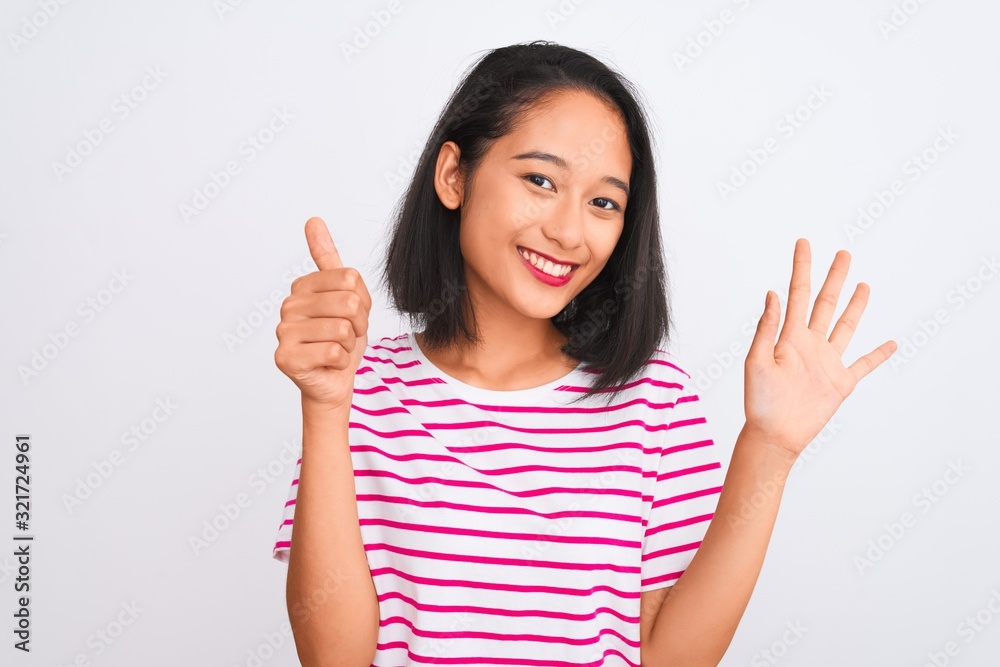 Young chinese woman wearing striped t-shirt standing over isolated white background showing and pointing up with fingers number six while smiling confident and happy. Young chinese woman wearing striped t-shirt standing over isolated white background showing and pointing up with fingers number six while smiling confident and happy.
