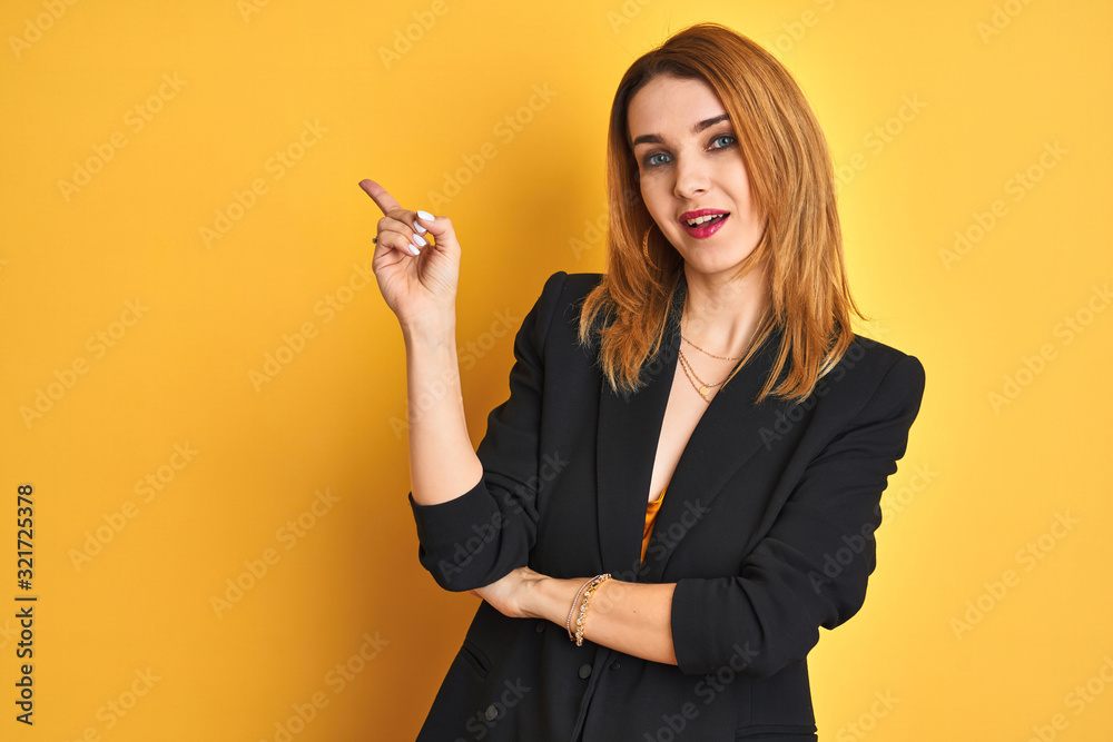 Redhead caucasian business woman over yellow isolated background with a big smile on face, pointing with hand and finger to the side looking at the camera. Redhead caucasian business woman over yellow isolated background with a big smile on face, pointing with hand and finger to the side looking at the camera.