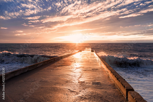 Big waves breaking on a stone pier in stormy weather with a bright sunset, a big tide. Black Sea. Sochi, February.