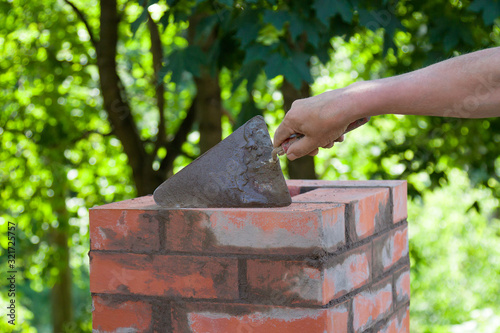 Fotografija Masonry works,  male hand working with a trowel, repairing a chimney from red br