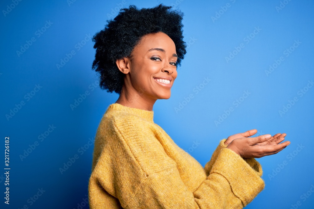 Young beautiful African American afro woman with curly hair wearing yellow casual sweater pointing aside with hands open palms showing copy space, presenting advertisement smiling excited happy Young beautiful African American afro woman with curly hair wearing yellow casual sweater pointing aside with hands open palms showing copy space, presenting advertisement smiling excited happy