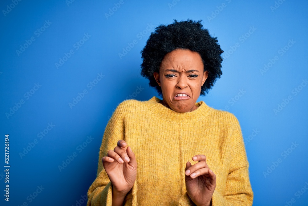 Fototapeta premium Young beautiful African American afro woman with curly hair wearing yellow casual sweater disgusted expression, displeased and fearful doing disgust face because aversion reaction.