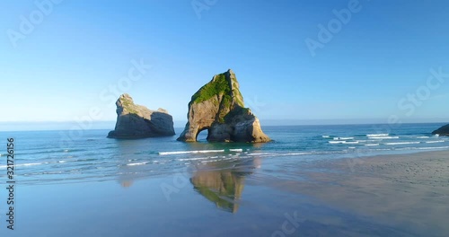 Aerial 4k forwartd tracking from low angle motion view of the rock formations of Archway Islands that sit just off shore of Wharariki Beach on the northern tip of the south island of New zealand photo