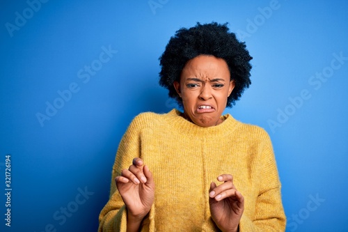 Fototapeta Young beautiful African American afro woman with curly hair wearing yellow casual sweater disgusted expression, displeased and fearful doing disgust face because aversion reaction