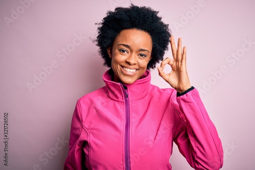 Young African American afro sportswoman with curly hair wearing sportswear doin sport smiling positive doing ok sign with hand and fingers. Successful expression.
