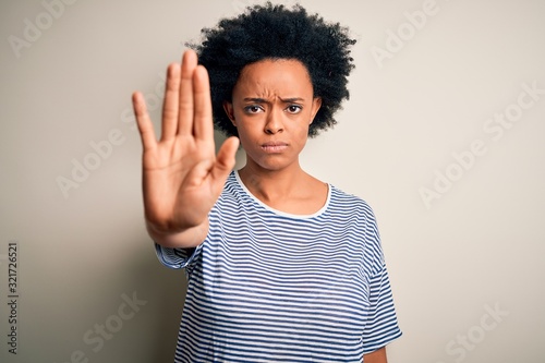 Young beautiful African American afro woman with curly hair wearing striped t-shirt doing stop sing with palm of the hand. Warning expression with negative and serious gesture on the face. © Krakenimages.com