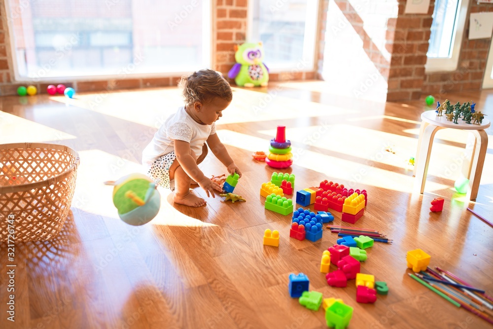 Adorable toddler playing with building blocks around lots of toys at kindergarten - obrazy, fototapety, plakaty 
