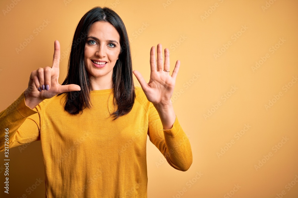 Young brunette woman with blue eyes wearing casual sweater over yellow background showing and pointing up with fingers number seven while smiling confident and happy. Young brunette woman with blue eyes wearing casual sweater over yellow background showing and pointing up with fingers number seven while smiling confident and happy.