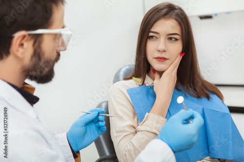 Attractive young woman suffering from toothache, visiting dentist at the clinic. Dental problems, aching teeth concept
