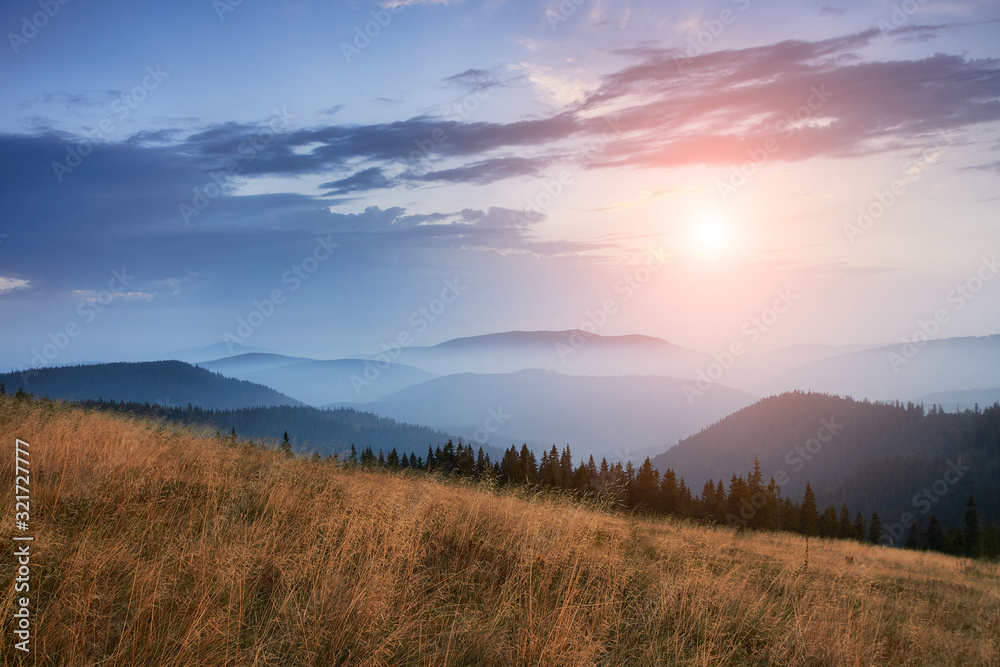 Majestic landscape of mountains at sunrise. View of the misty tops and layer hills of the mountains in the distance. Dramatic sky and rays of sunlight at morning. Concept of nature background. Majestic landscape of mountains at sunrise. View of the misty tops and layer hills of the mountains in the distance. Dramatic sky and rays of sunlight at morning. Concept of nature background.